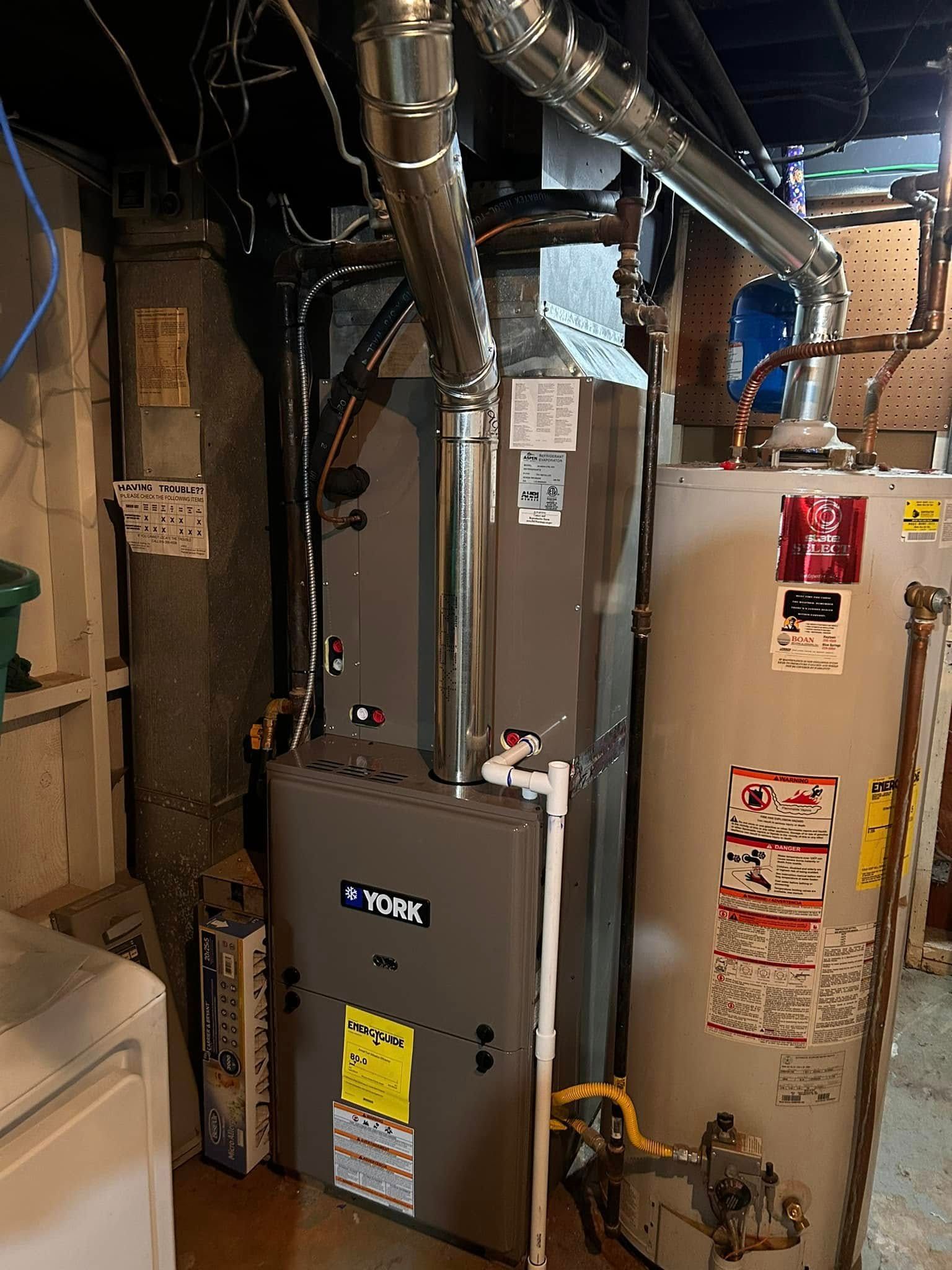 Furnace and water heater in a basement utility room with ductwork and pipes.