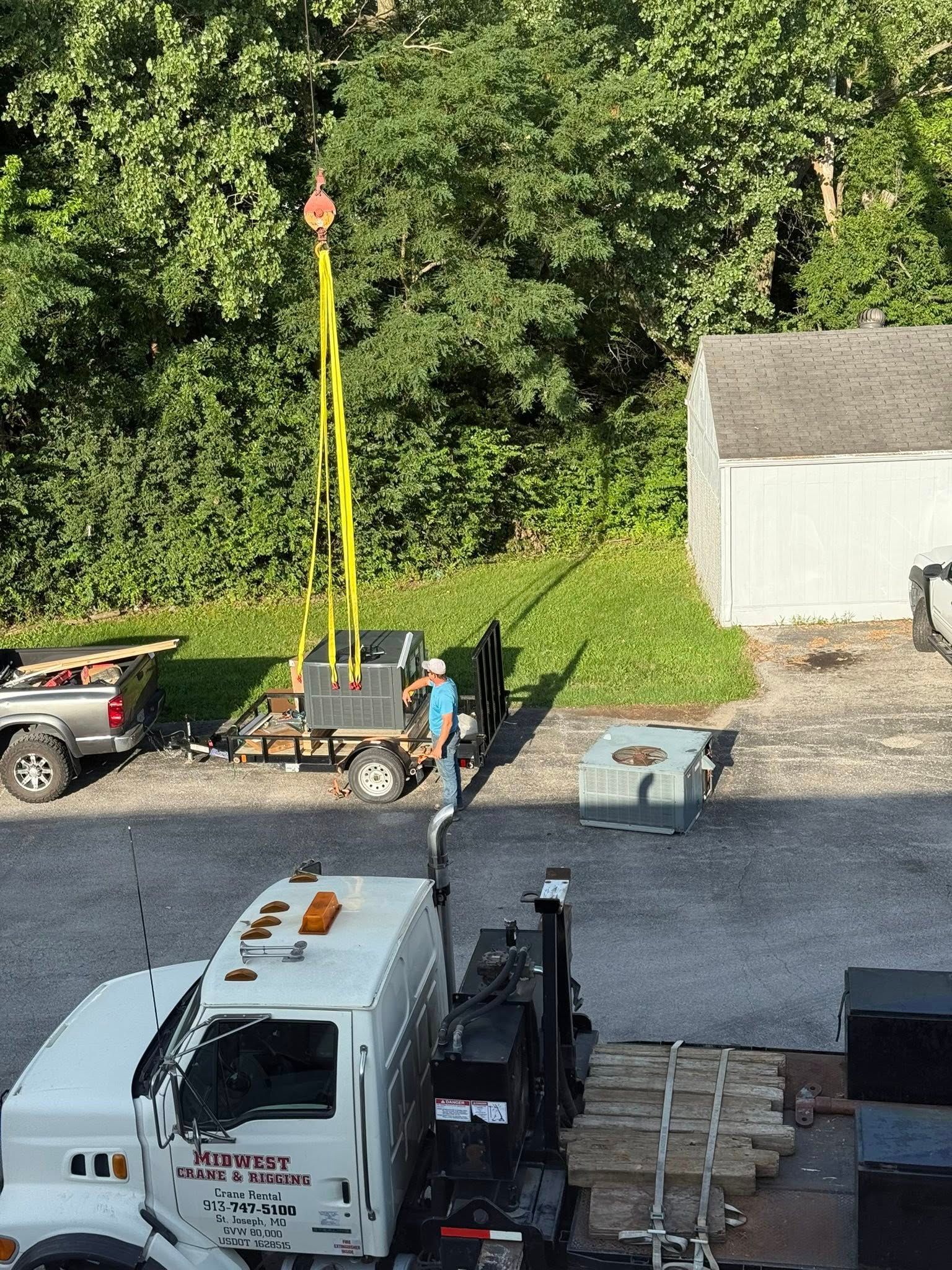 Crane lifting equipment from a trailer. Trucks and trees are in the background.