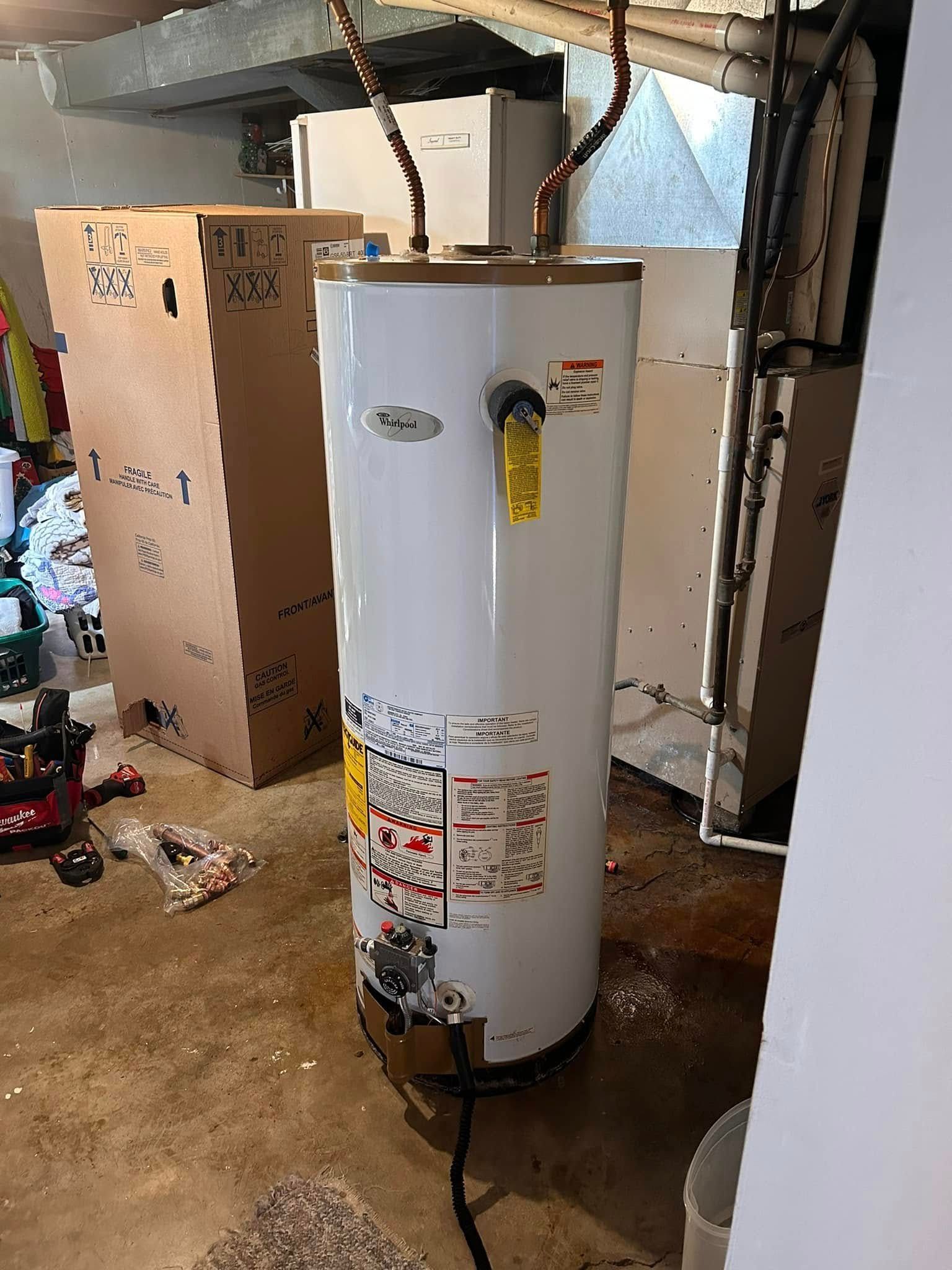 A tall, white water heater in a basement setting with copper pipes and electrical wiring.