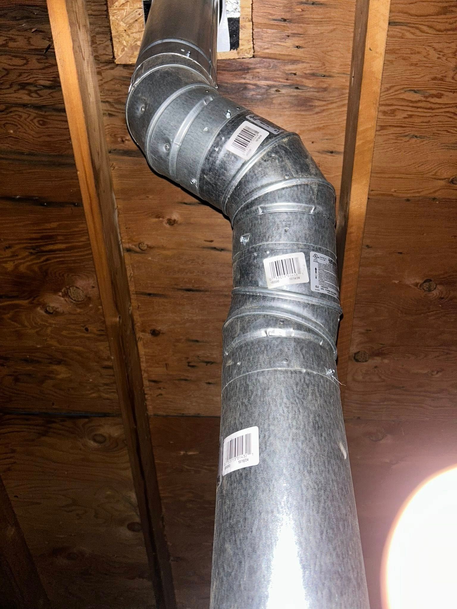 Metal ductwork runs through a wooden attic, curved with labels attached.