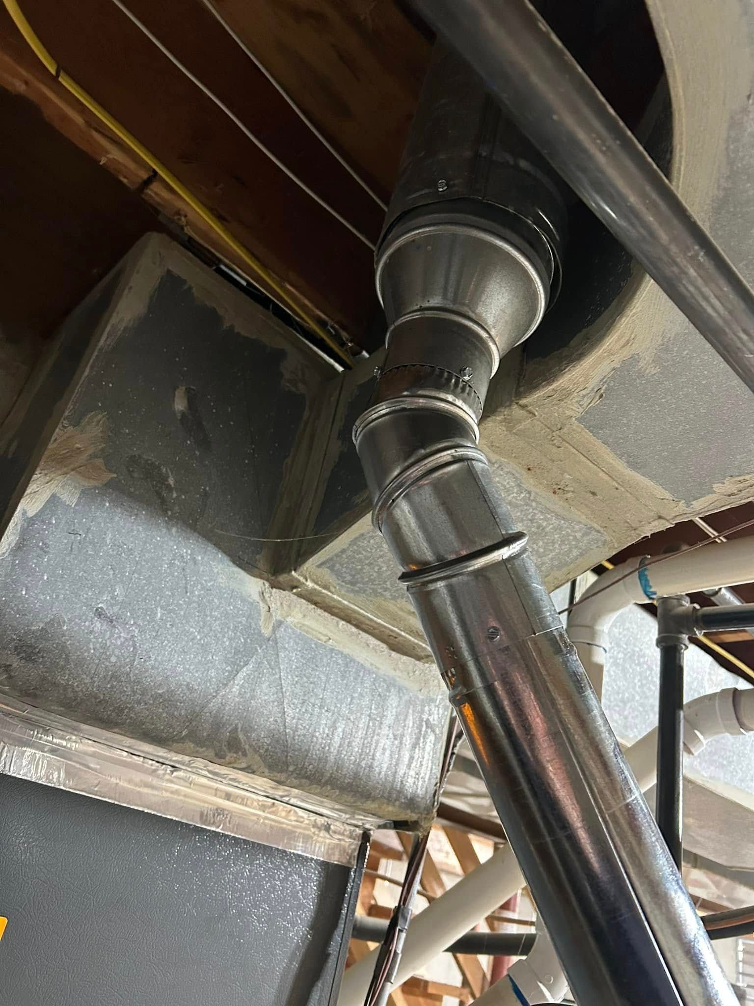 Silver HVAC ductwork angled through a ceiling, connecting to a larger rectangular duct.