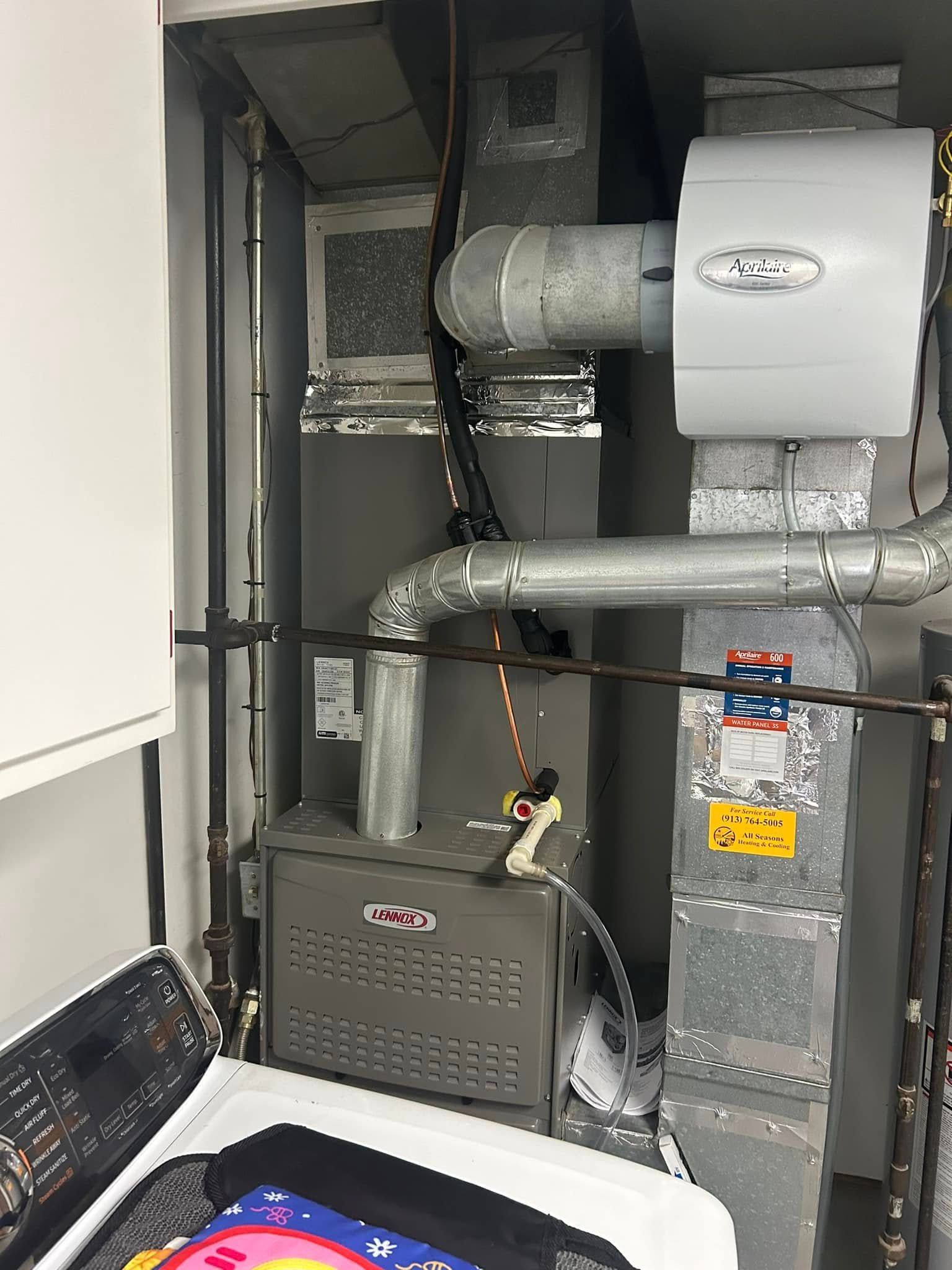 Furnace and humidifier in a utility room with ductwork and laundry appliances.