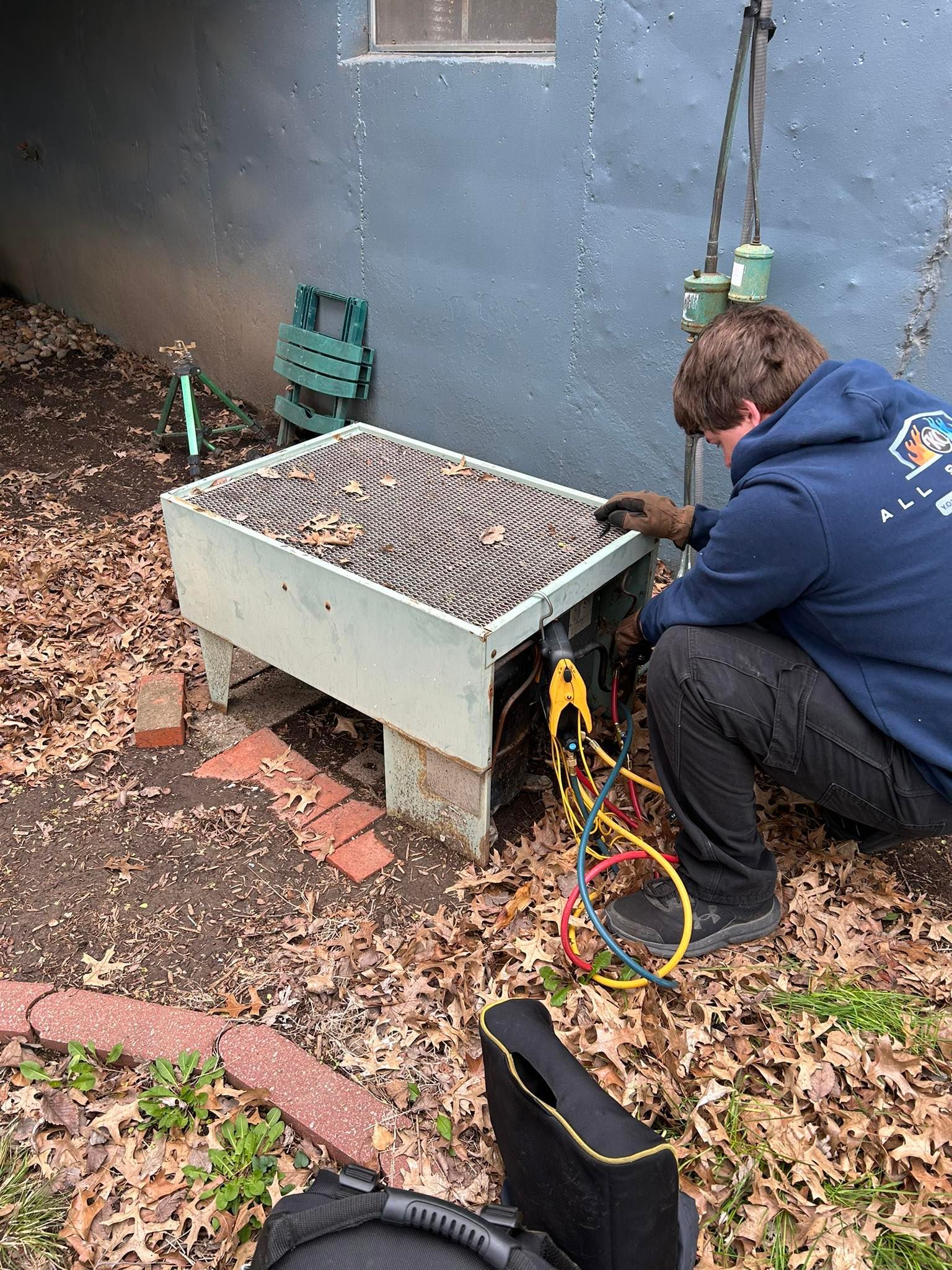 HVAC technician working on an outside air conditioning unit. He is using a multimeter with wires attached.