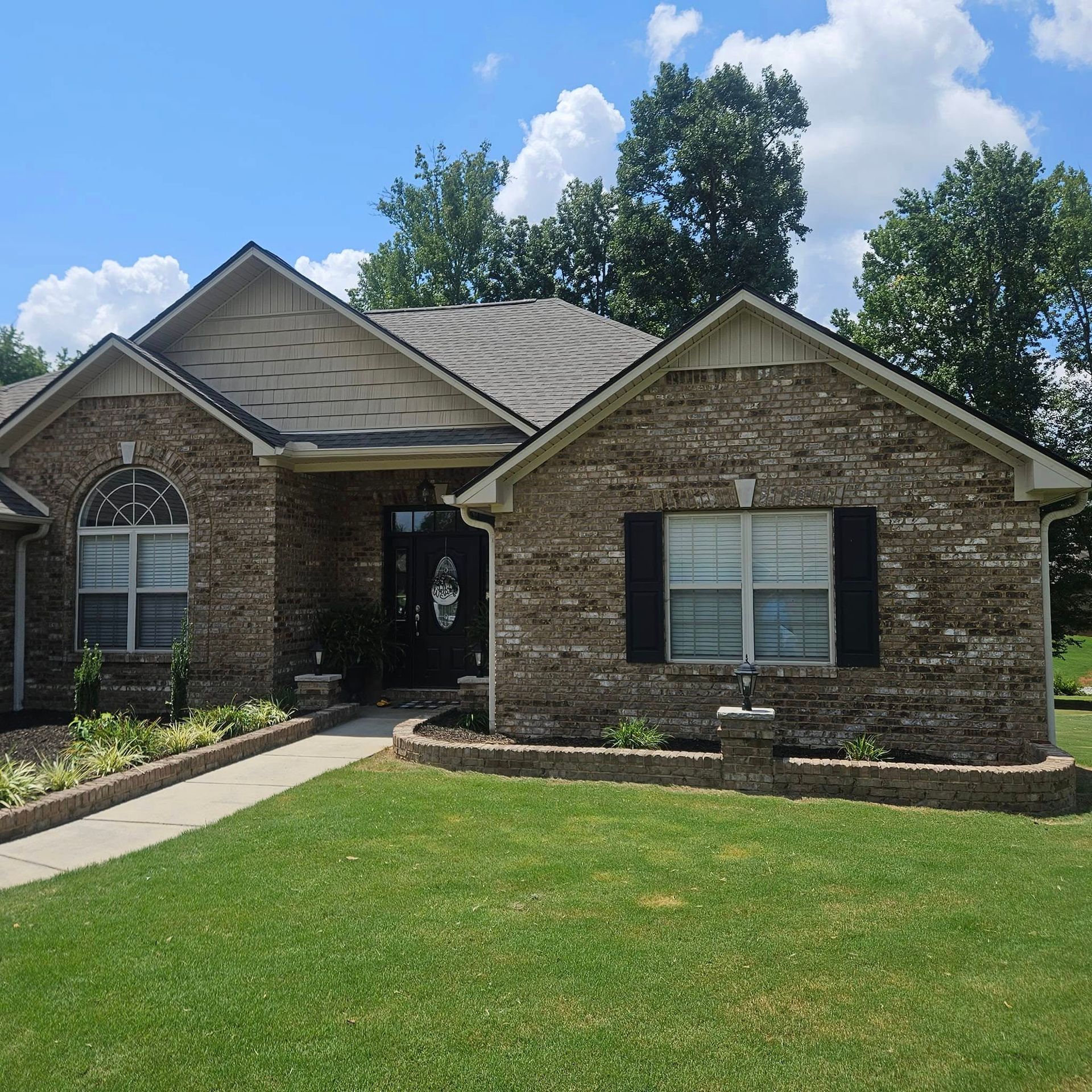 Aerial view of a multi-gabled house roof with layered grey and brown shingles under clear skies.