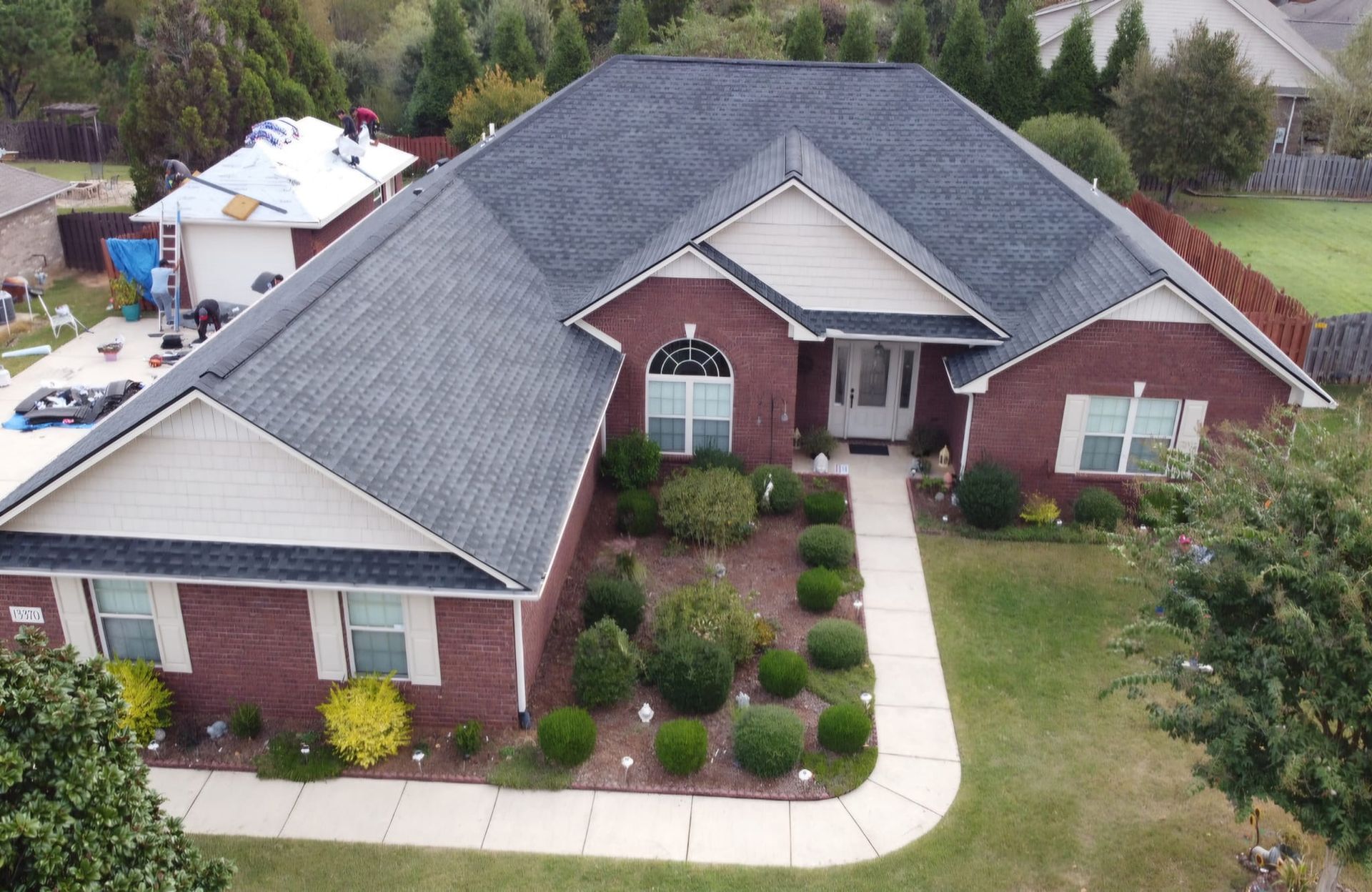 A person uses a yellow pneumatic roofing nailer to attach asphalt shingles to a roof.