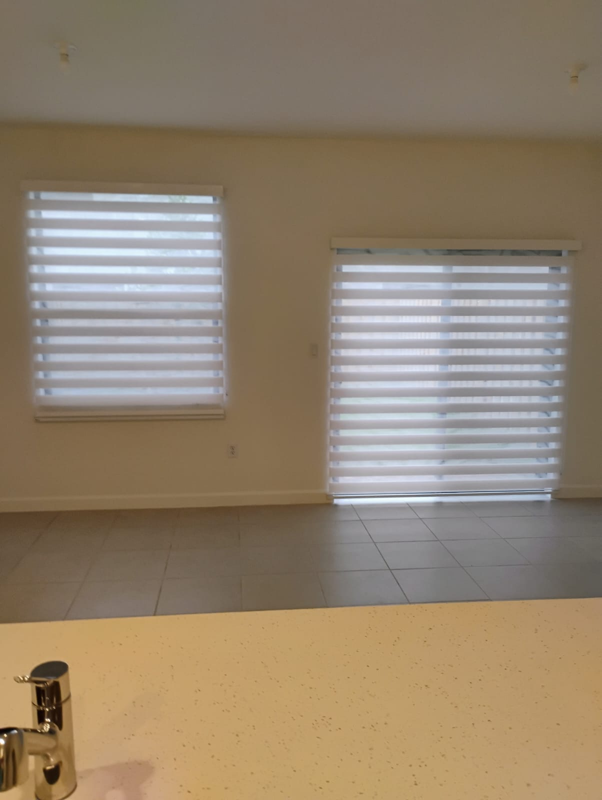 Interior view with window and sliding door covered by zebra blinds in a room with tiled floor.