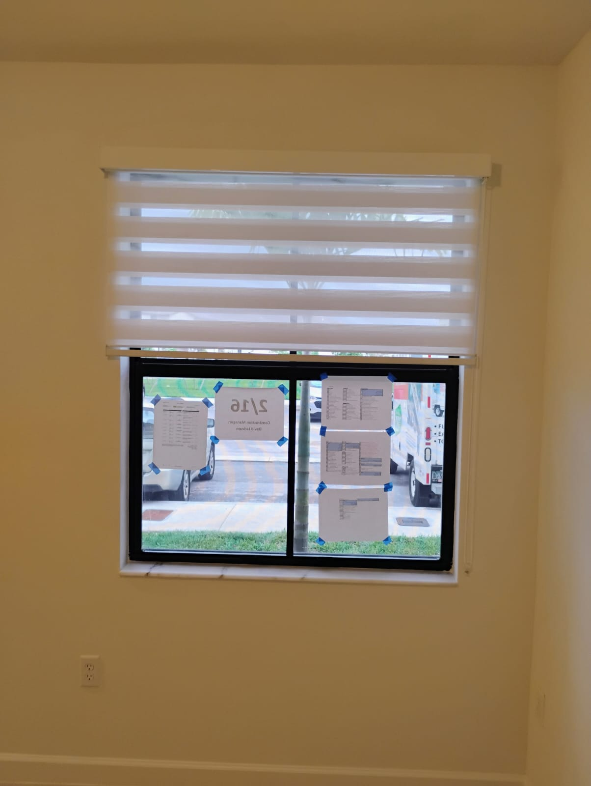 Window with layered sheer blinds. Paper notes taped to the glass, beige walls.