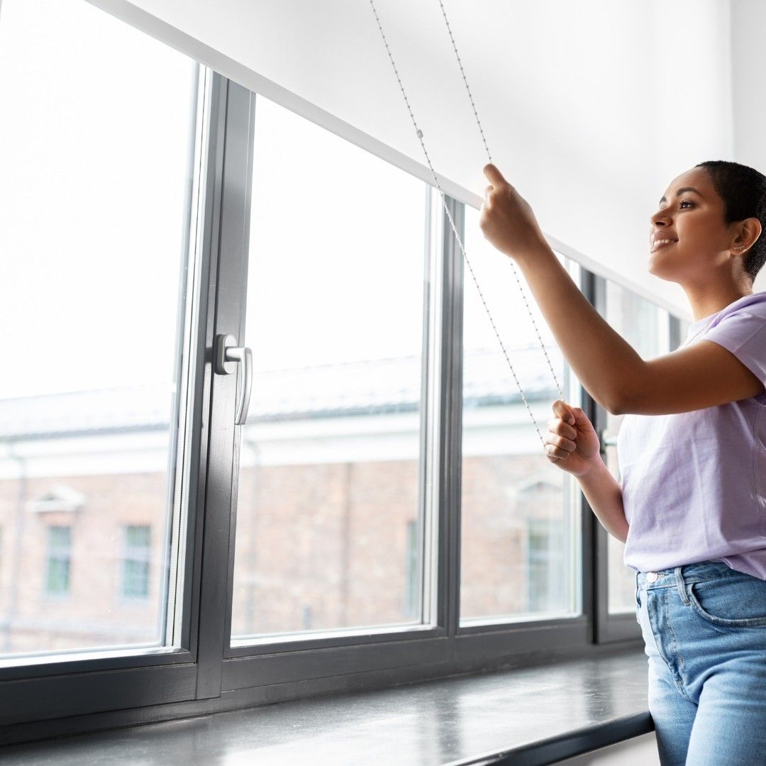 Woman pulling the cord of a window shade in a bright room.