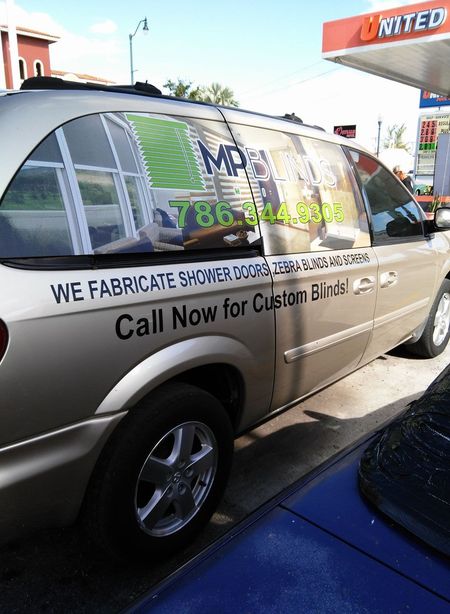 Gold minivan with business advertisement for shower doors and blinds at a gas station.