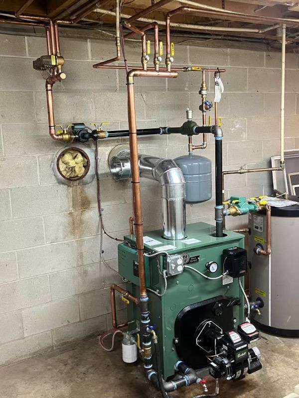 Green boiler system with copper pipes, installed against a concrete block wall.