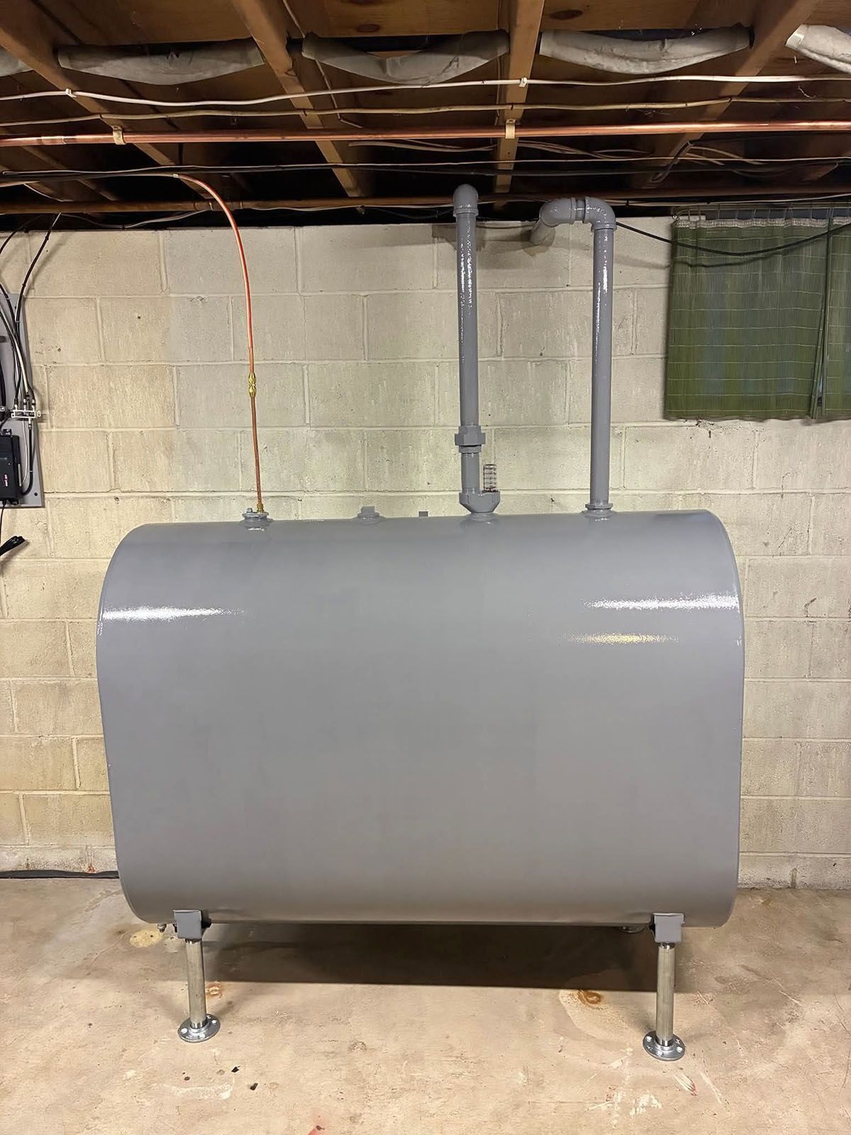 A grey oil tank with pipes in a basement against a cinder block wall