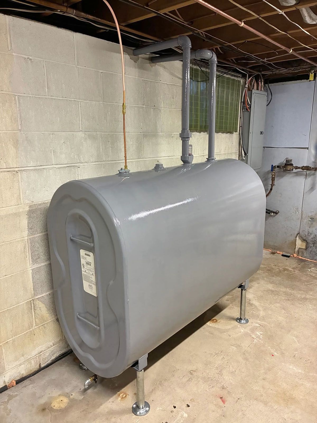 A gray oil tank with connected pipes in a basement