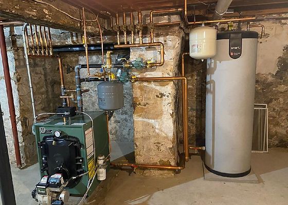 Heating system with boiler, pipes, water heater, and expansion tank against a stone wall.