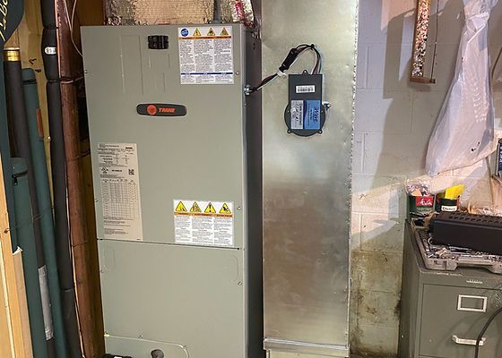 A gray HVAC system in a basement setting with ductwork.