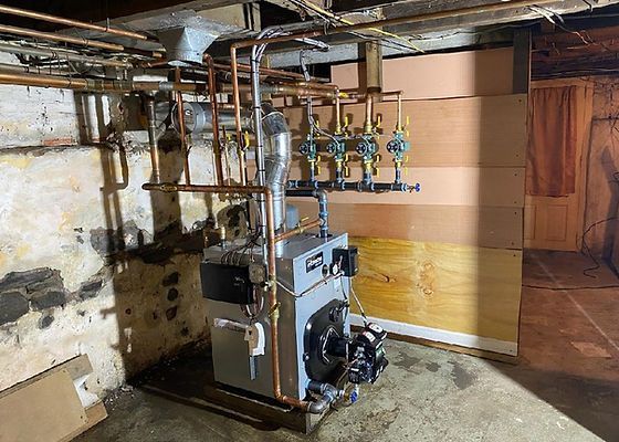 Boiler system in a basement with copper pipes, valves, and exposed insulation.
