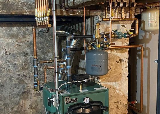 Green boiler with copper pipes and a blue expansion tank in a basement.