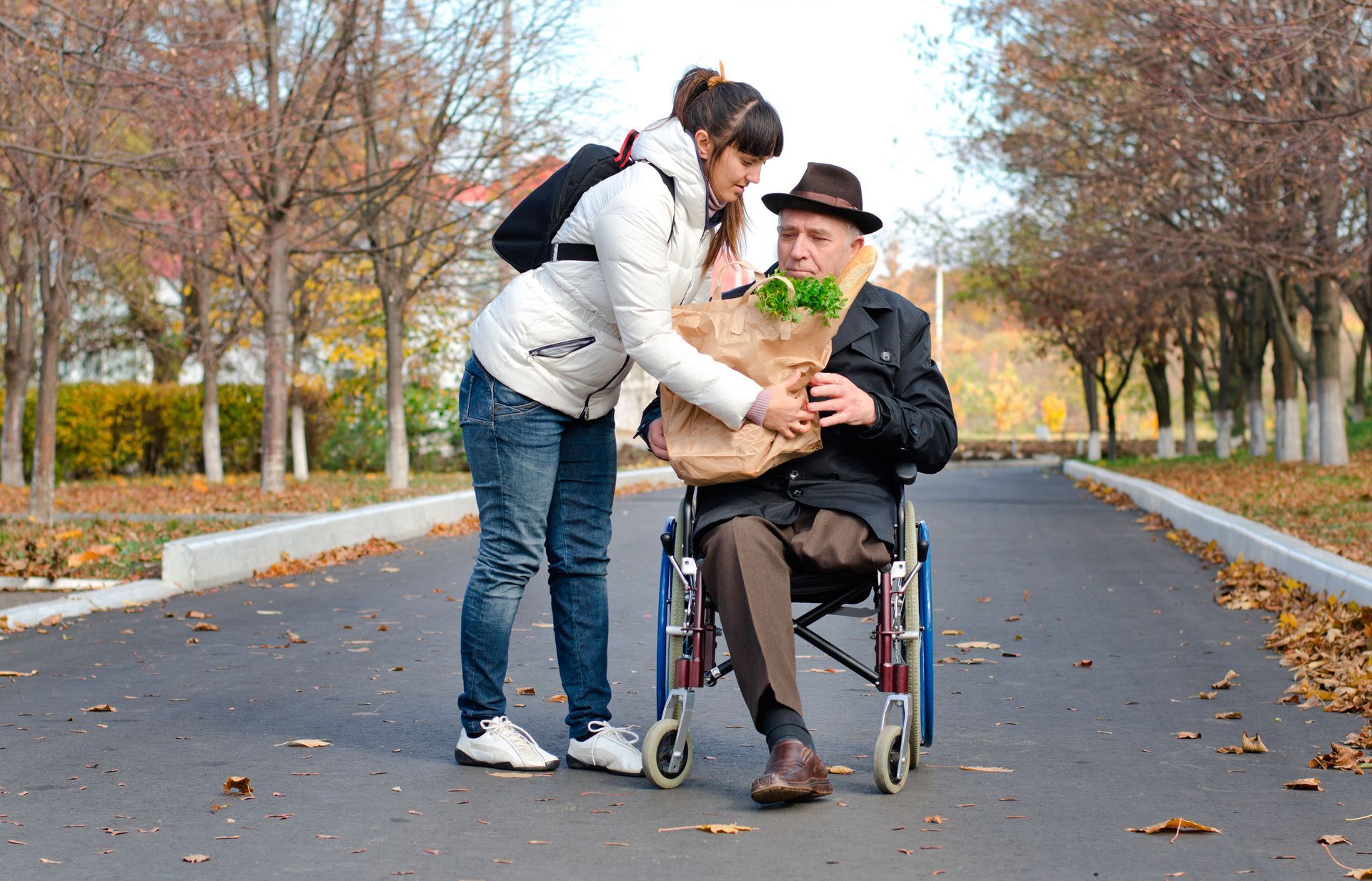A woman is helping an elderly man in a wheelchair with a bag of vegetables.