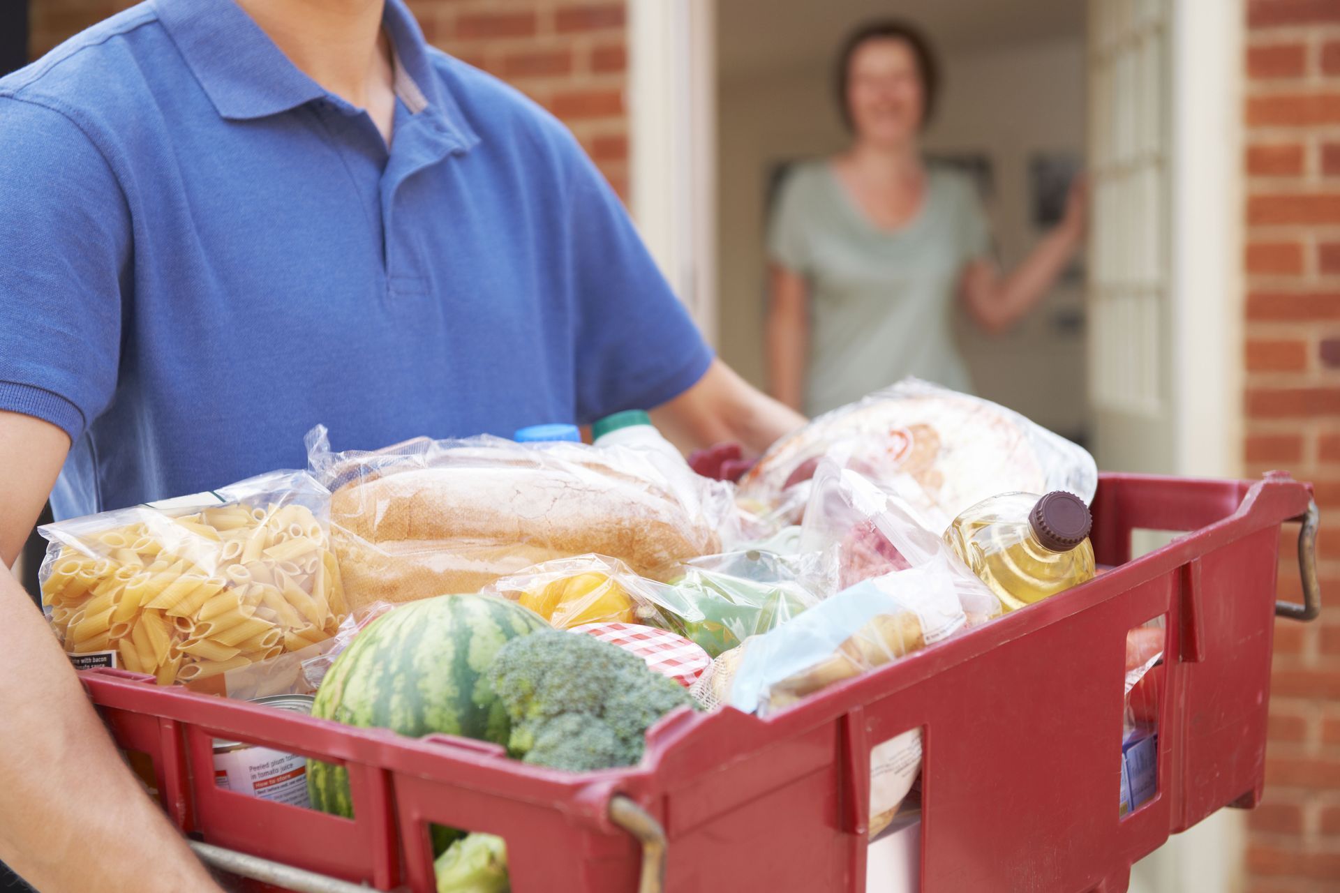 A man is carrying a crate of groceries to a woman.