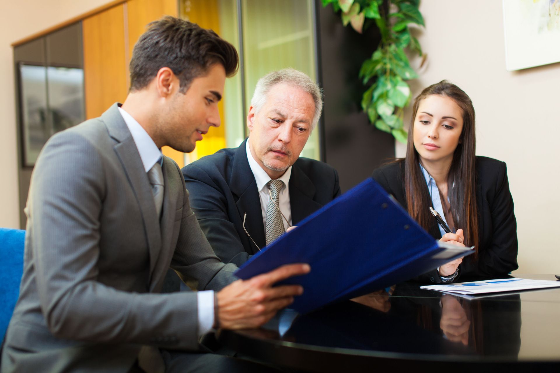 A group of business people are sitting around a table looking at a clipboard.