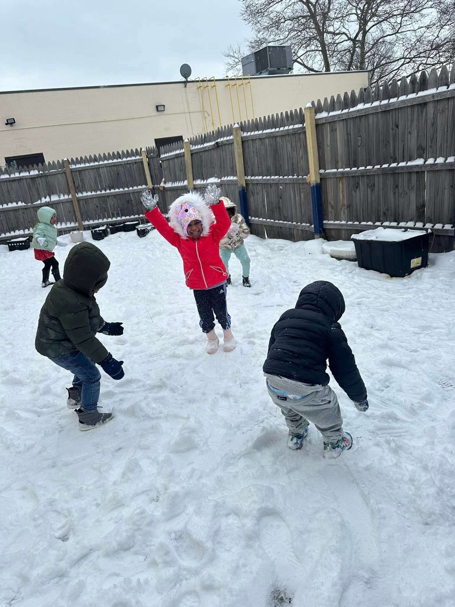 Children playing in the snow in a fenced yard. Some are throwing snowballs, others are laughing with joy.