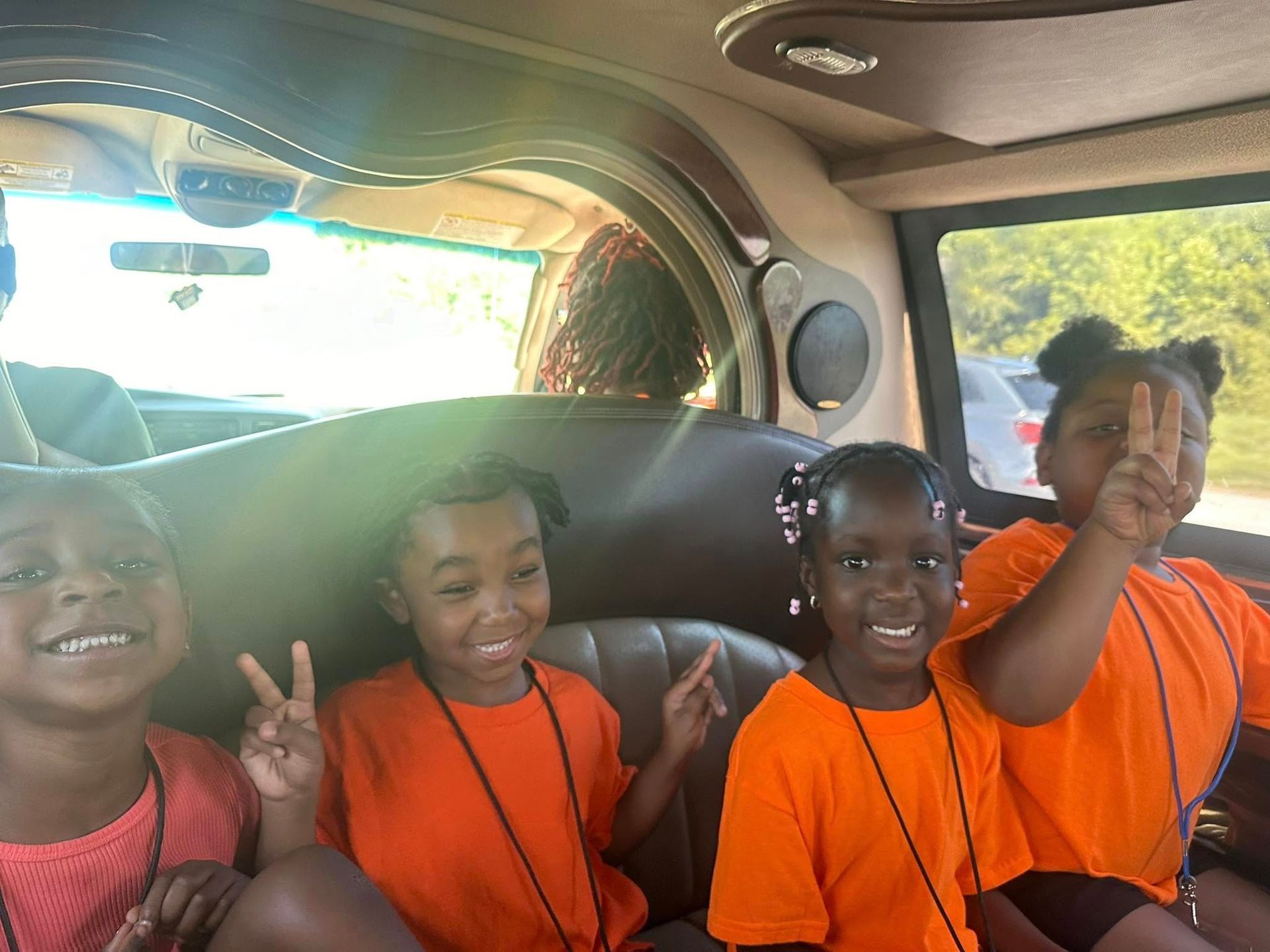 Four smiling girls in orange shirts pose inside a limo, giving peace signs.