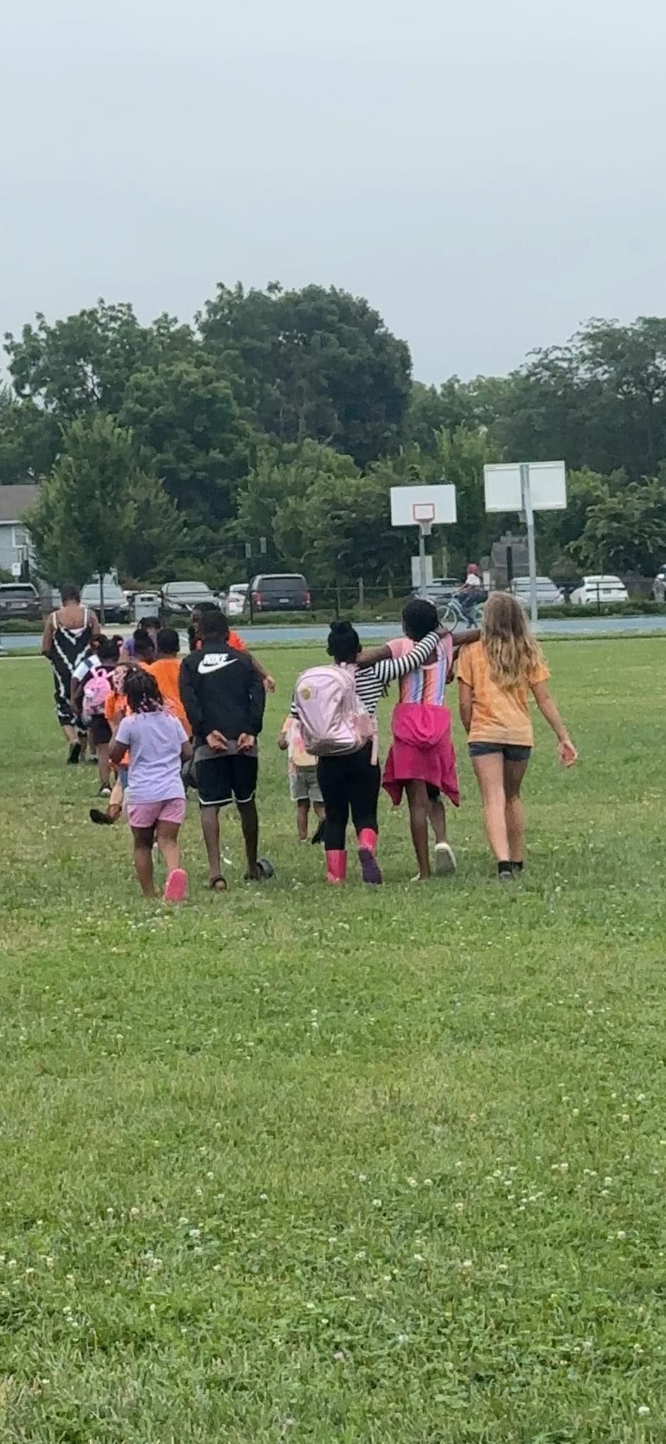 Children walking on a grassy field toward basketball hoops. Overcast day.