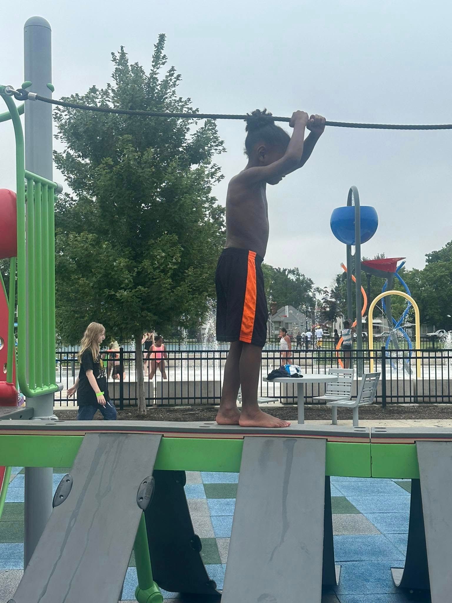 Boy holding onto a bar on a playground structure near a water park.