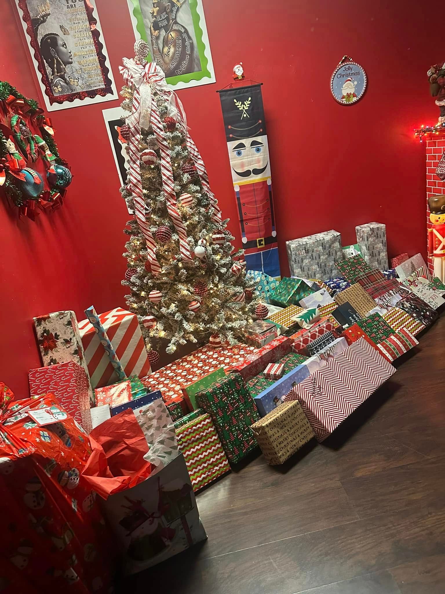 A Christmas tree surrounded by many wrapped gifts on a red-painted wall background.