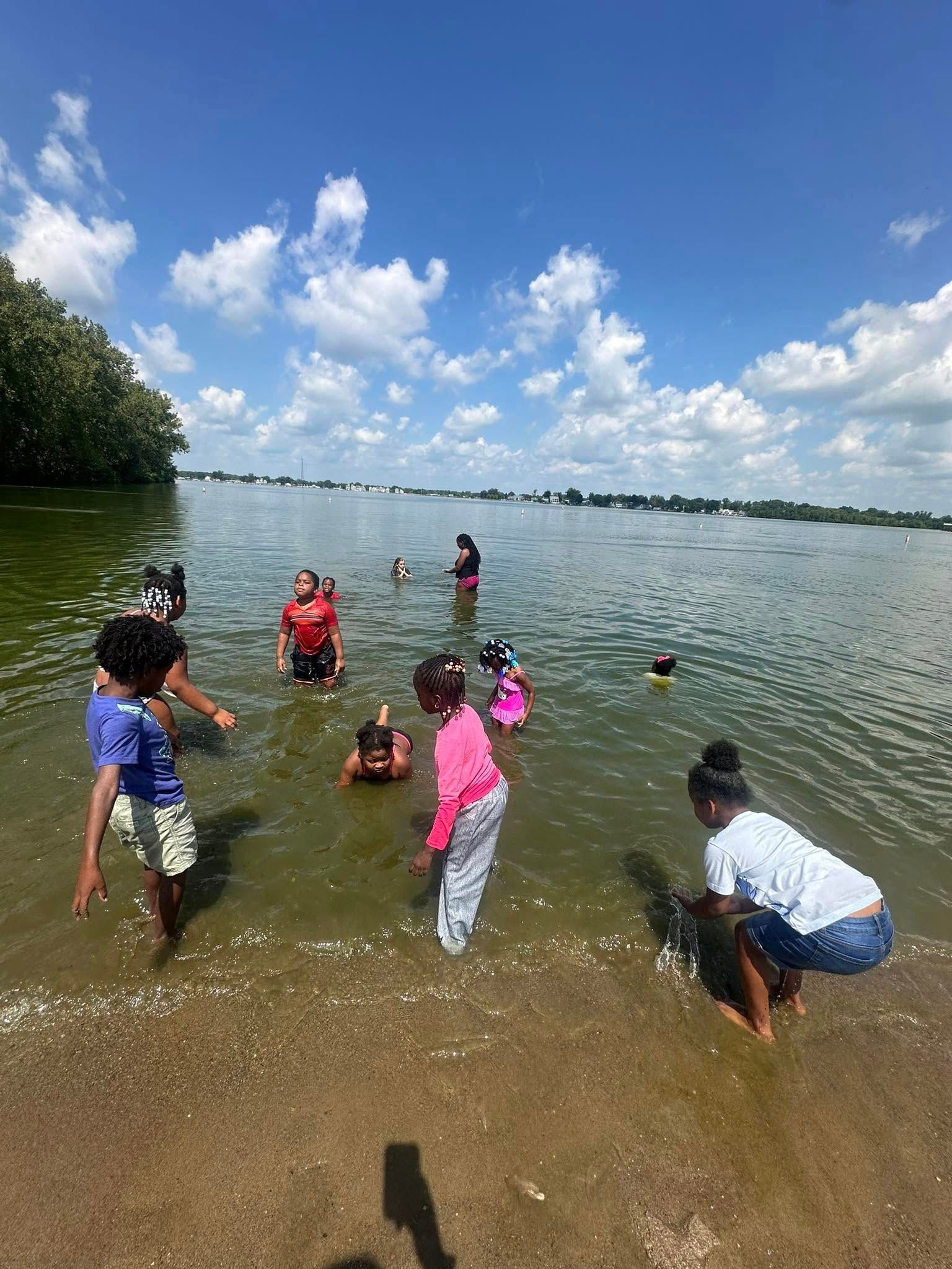 Children playing in shallow water at a beach on a sunny day; blue sky, clouds.