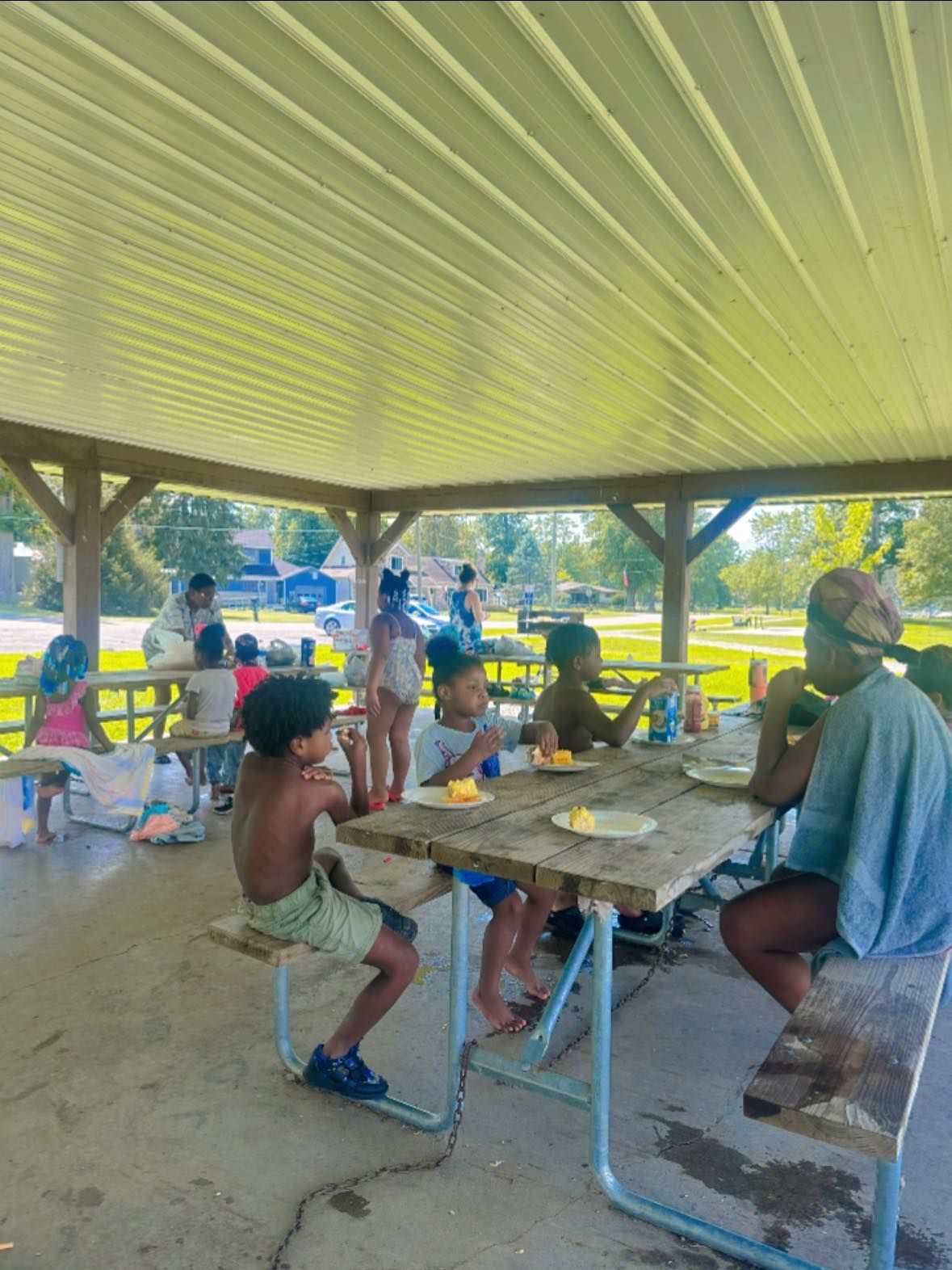 Children eating at picnic tables under a covered pavilion.
