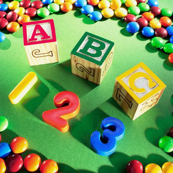 Alphabet blocks A, B, and C with colorful candy and numbers 1, 2, and 3 on a green surface.