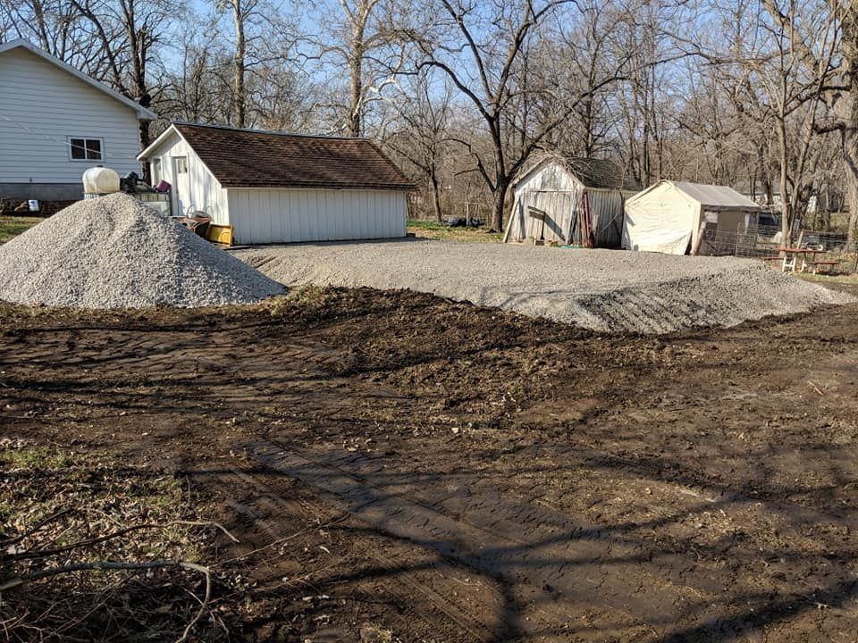 A pile of gravel is sitting in the middle of a dirt field in front of a house.