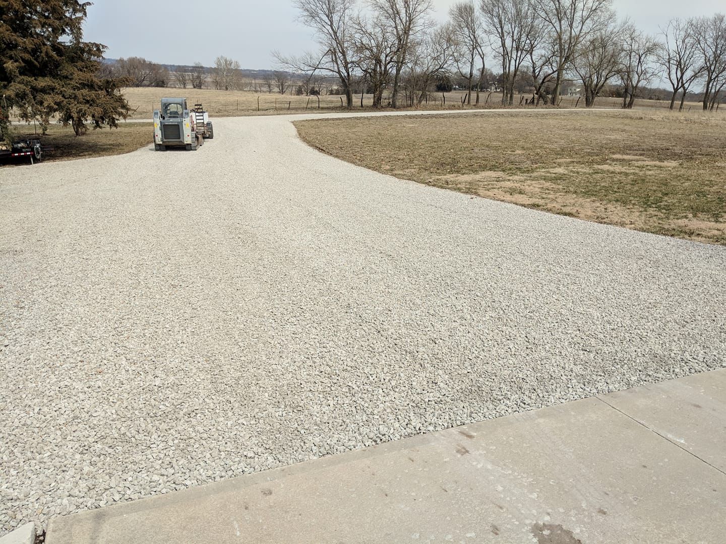 A gravel driveway leading to a field with trees in the background