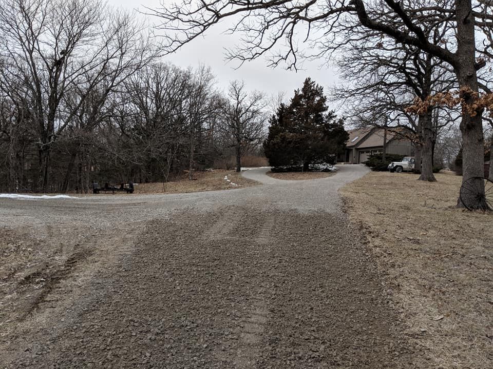 A dirt road with a house in the background and trees on the side.