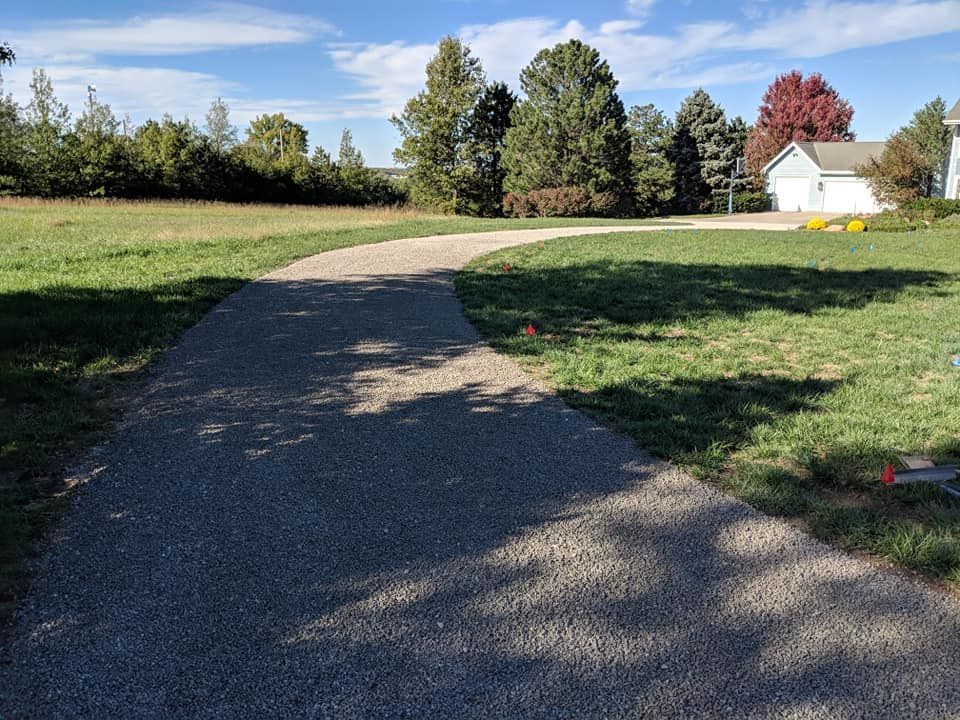 A dirt road going through a grassy field with a house in the background.