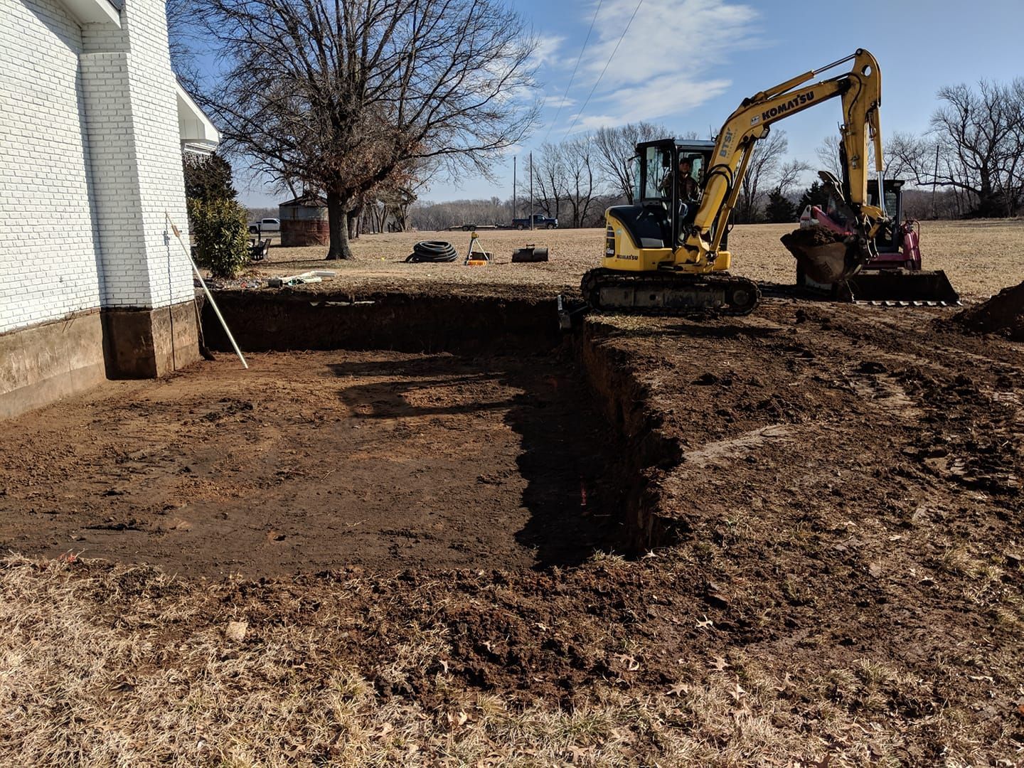 A yellow excavator is digging a hole in the ground in front of a house.