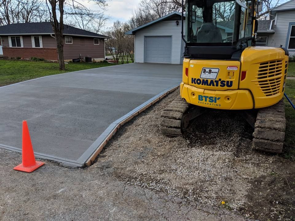 A yellow komatsu excavator is parked in a driveway next to an orange cone.