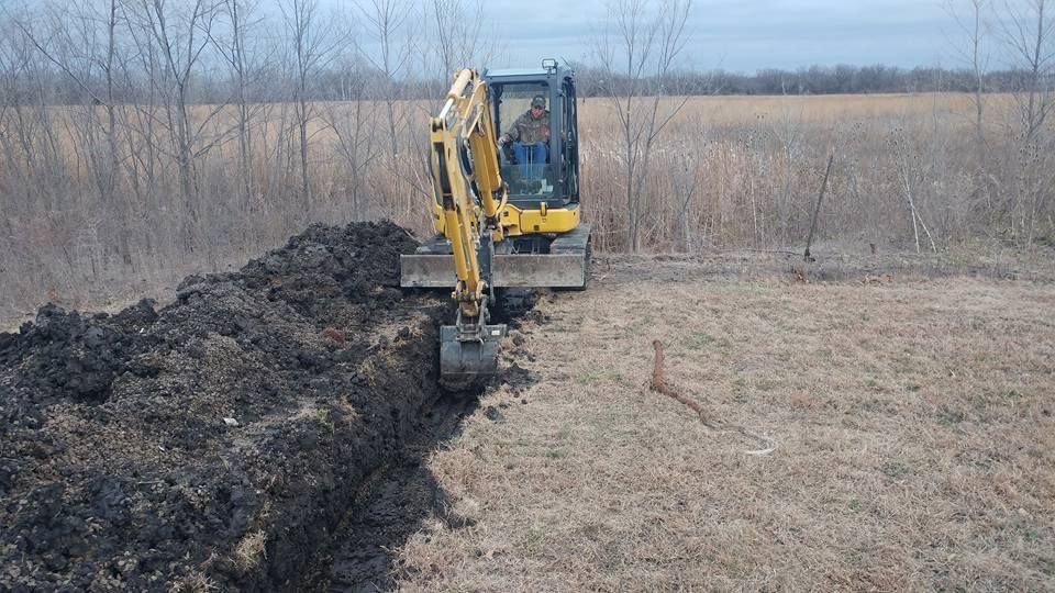 A yellow excavator is digging a trench in a field.