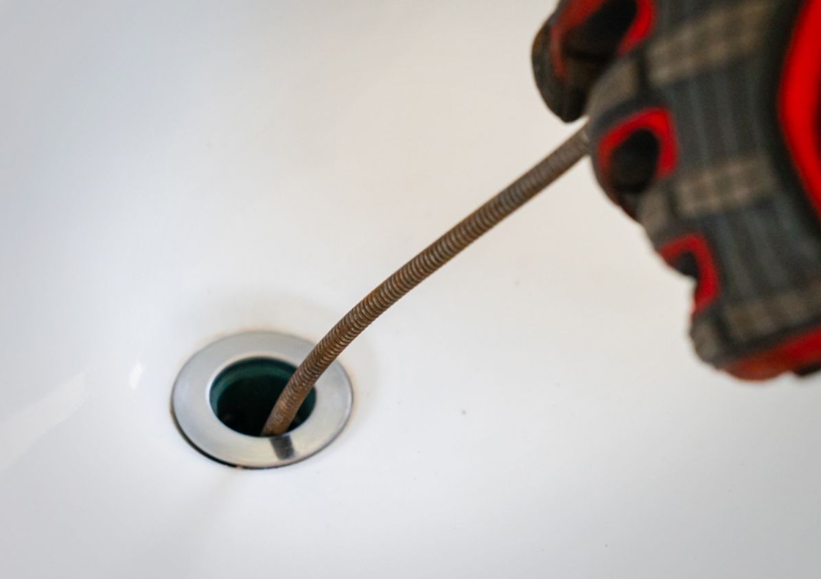 A person is using a hose to clean a sink drain.