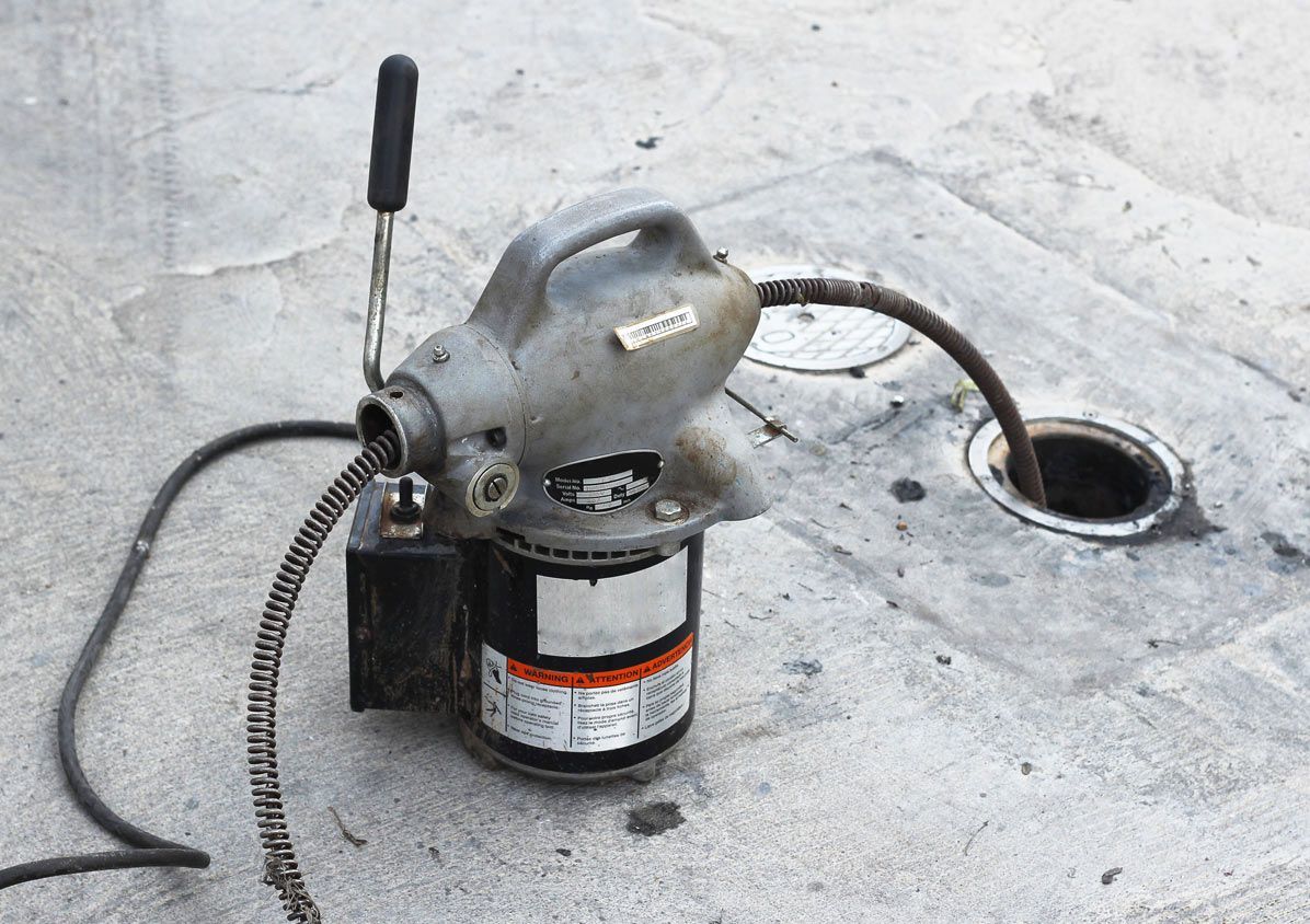 A drain cleaner is sitting on the ground next to a manhole cover.