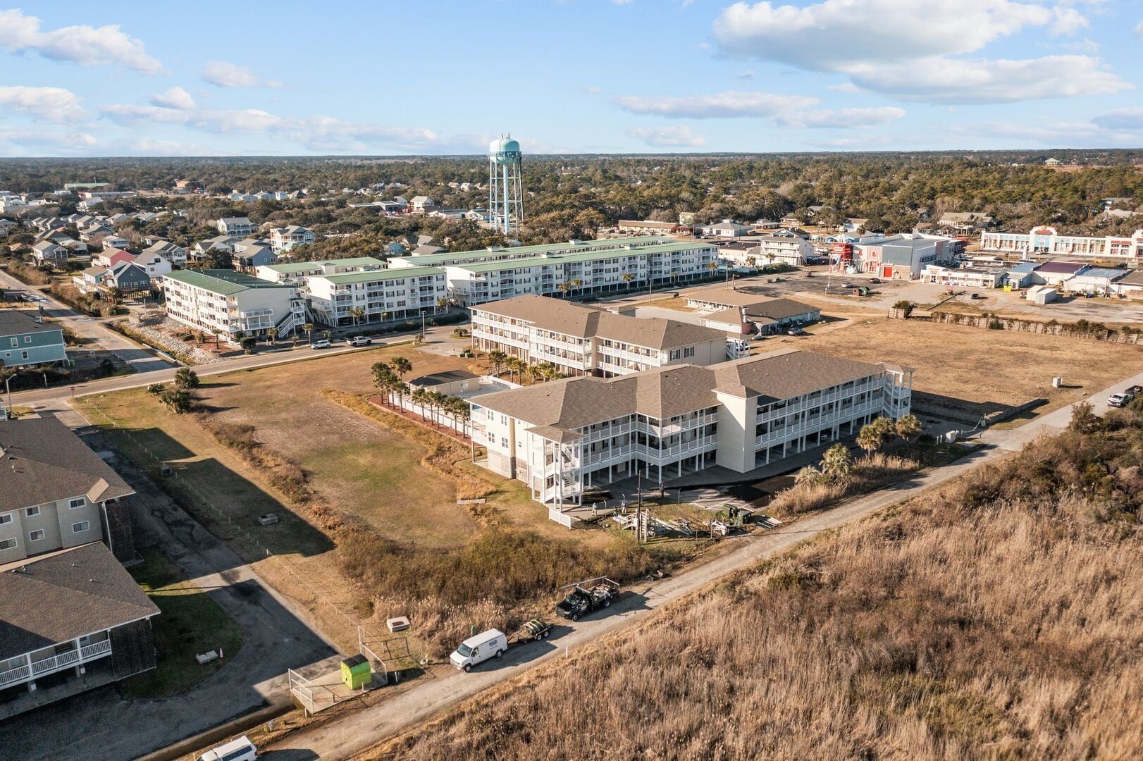 Aerial view of a coastal apartment complex under construction beside a grassy field and road
