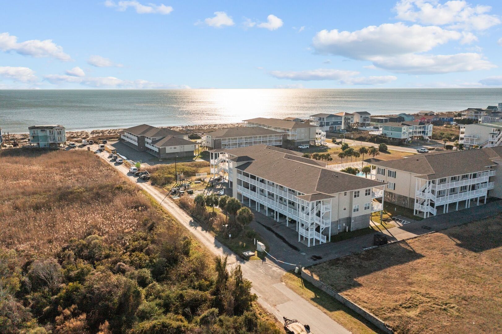 Coastal apartment buildings beside a road, with marshland and the ocean under a bright sky