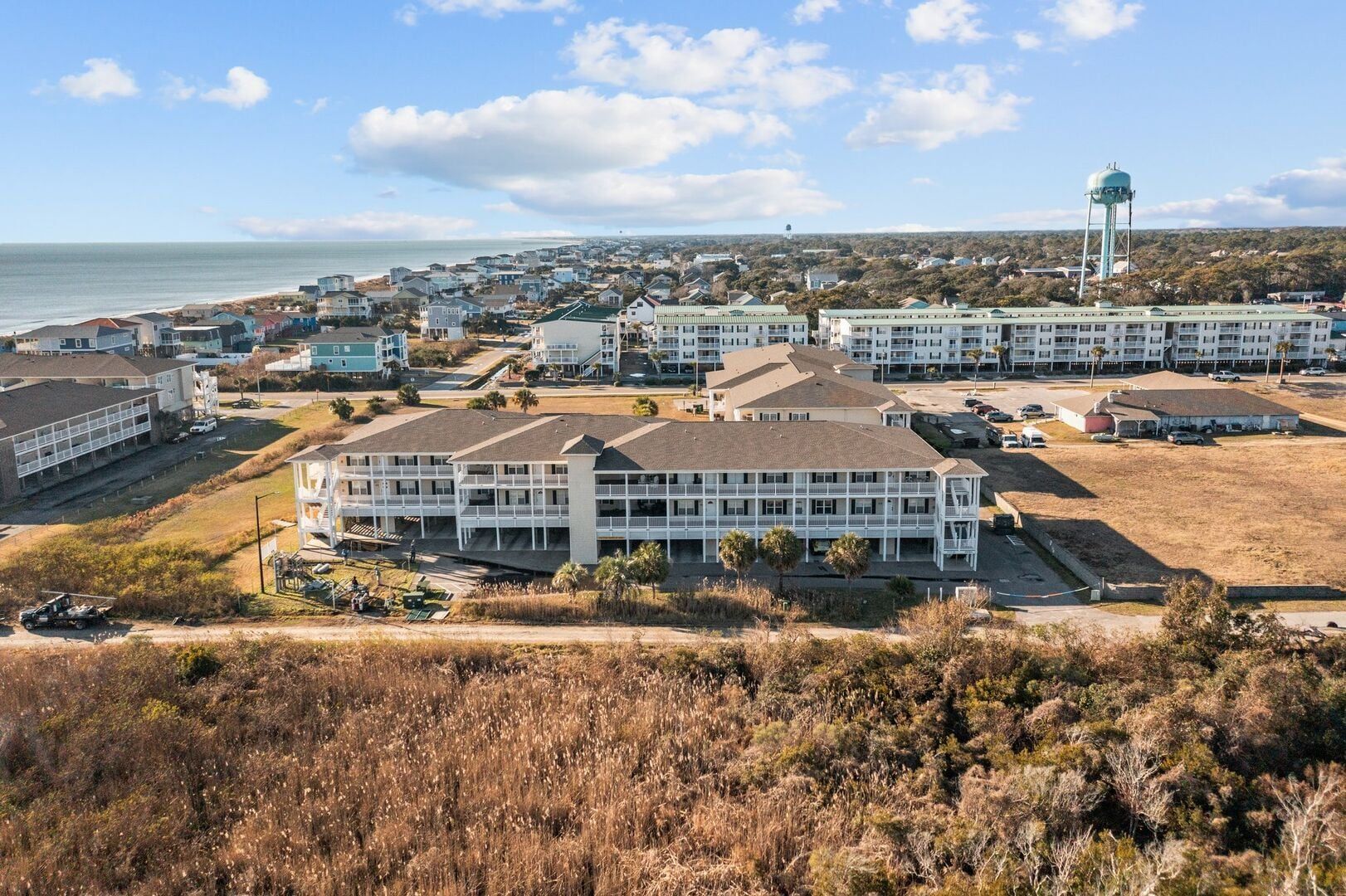 Coastal resort buildings with a water tower, viewed from a grassy dune near the ocean