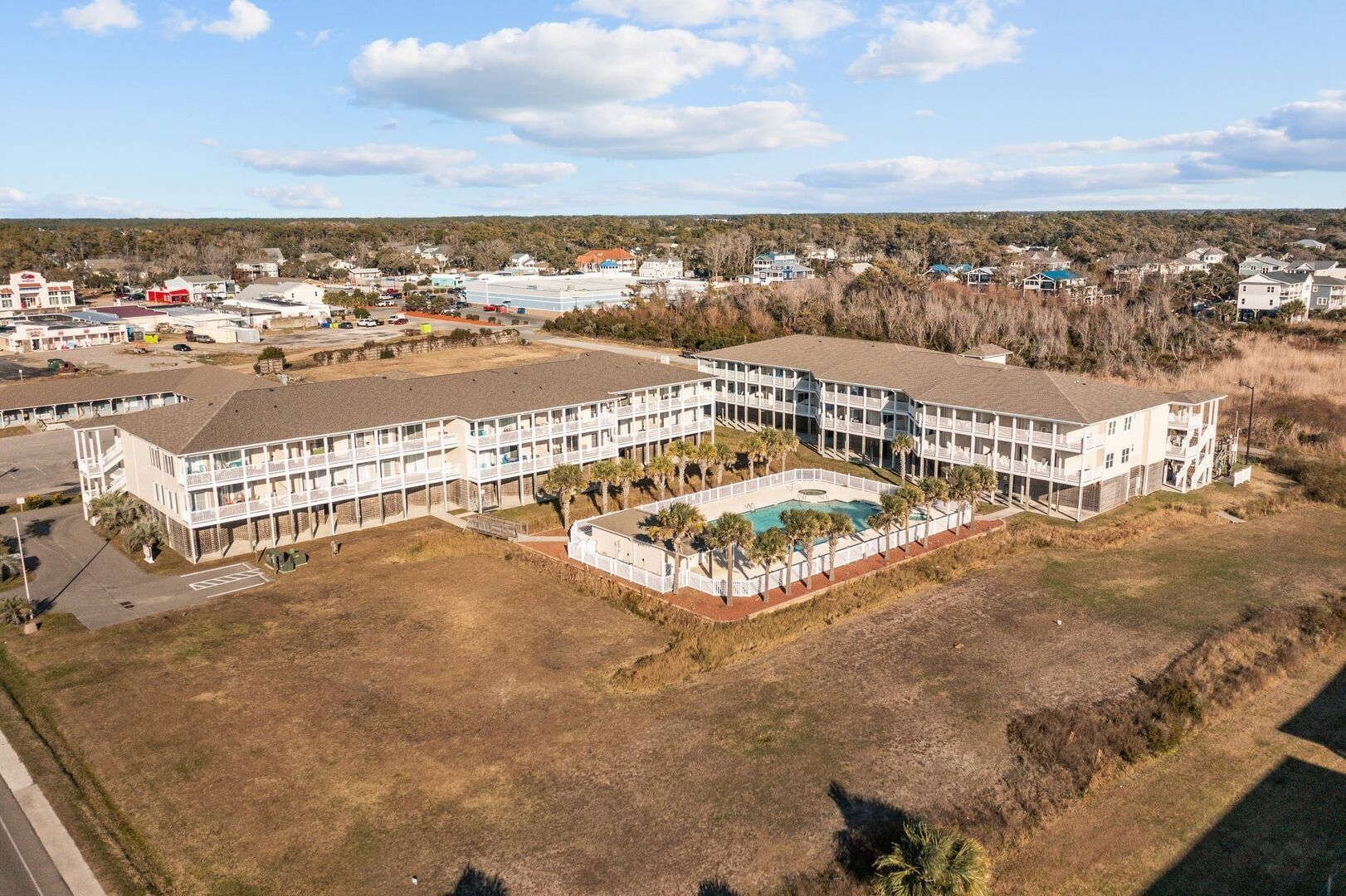 Aerial view of a white apartment complex with a central courtyard pool and surrounding brown fields.