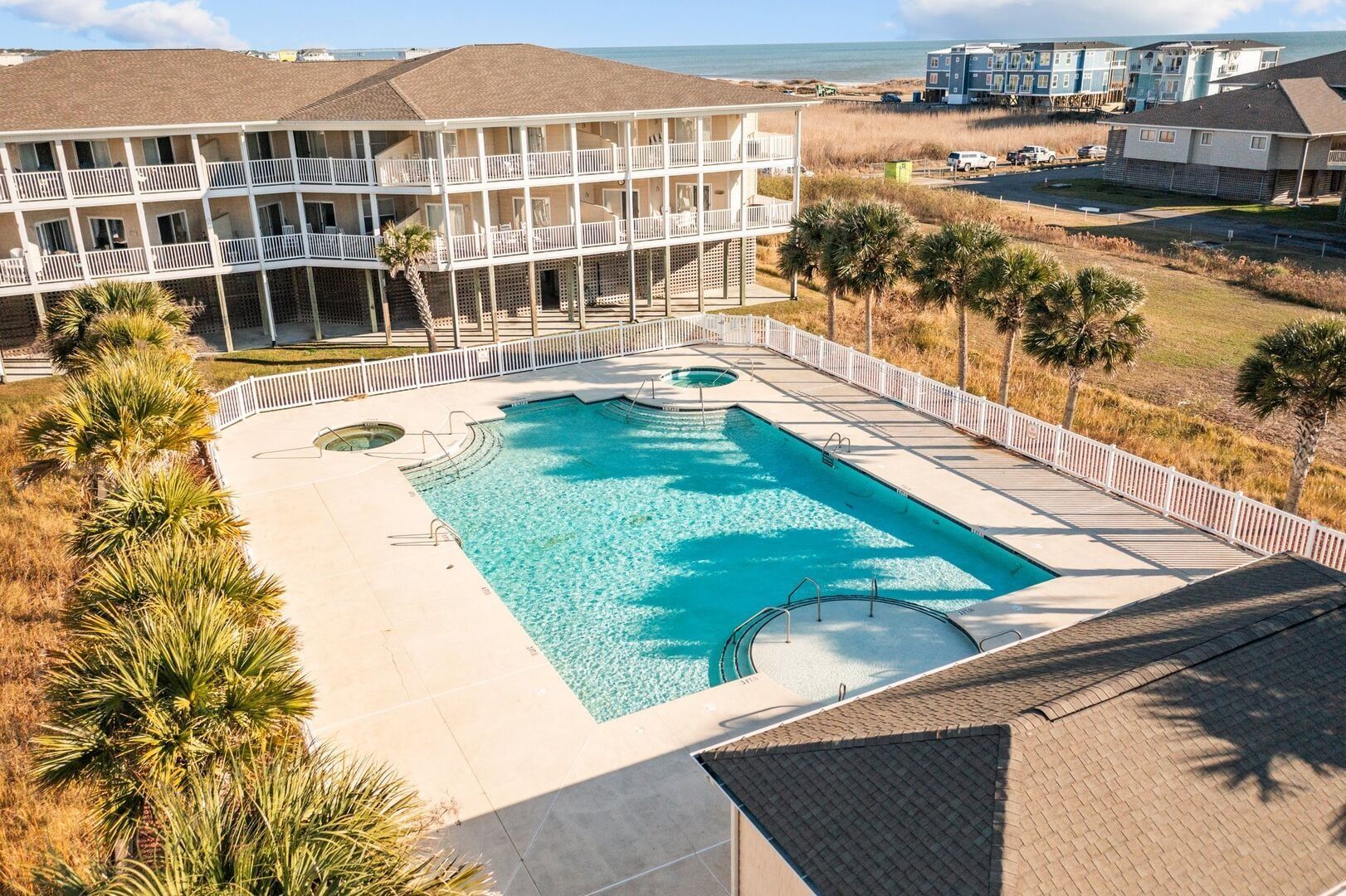 Apartment complex with a large turquoise pool and sun deck, viewed from above