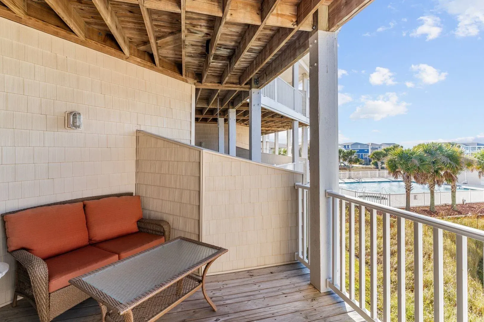 Covered balcony with orange sofa, table, and railings overlooking a waterfront view