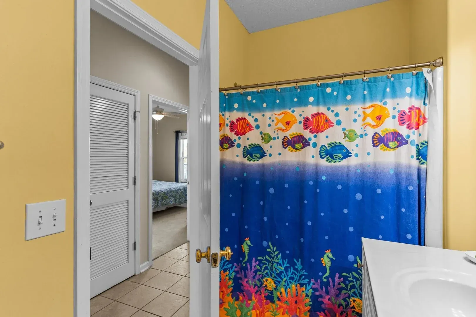 Bathroom with bright fish shower curtain, tiled floor, and open door to adjacent room