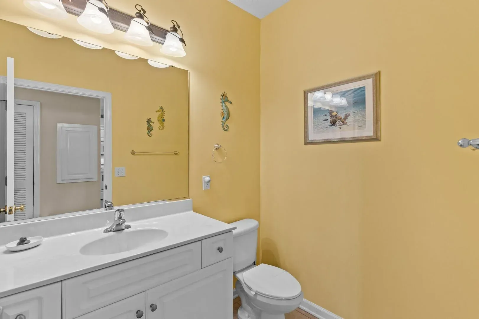 Yellow bathroom with white vanity, large mirror, toilet, and framed wall art