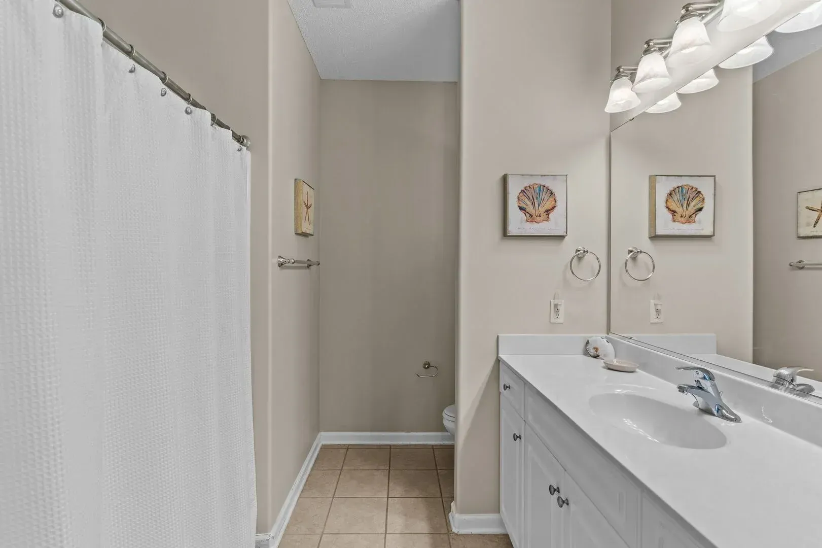 Bright bathroom with white vanity, large mirror, and shower curtain along the left wall