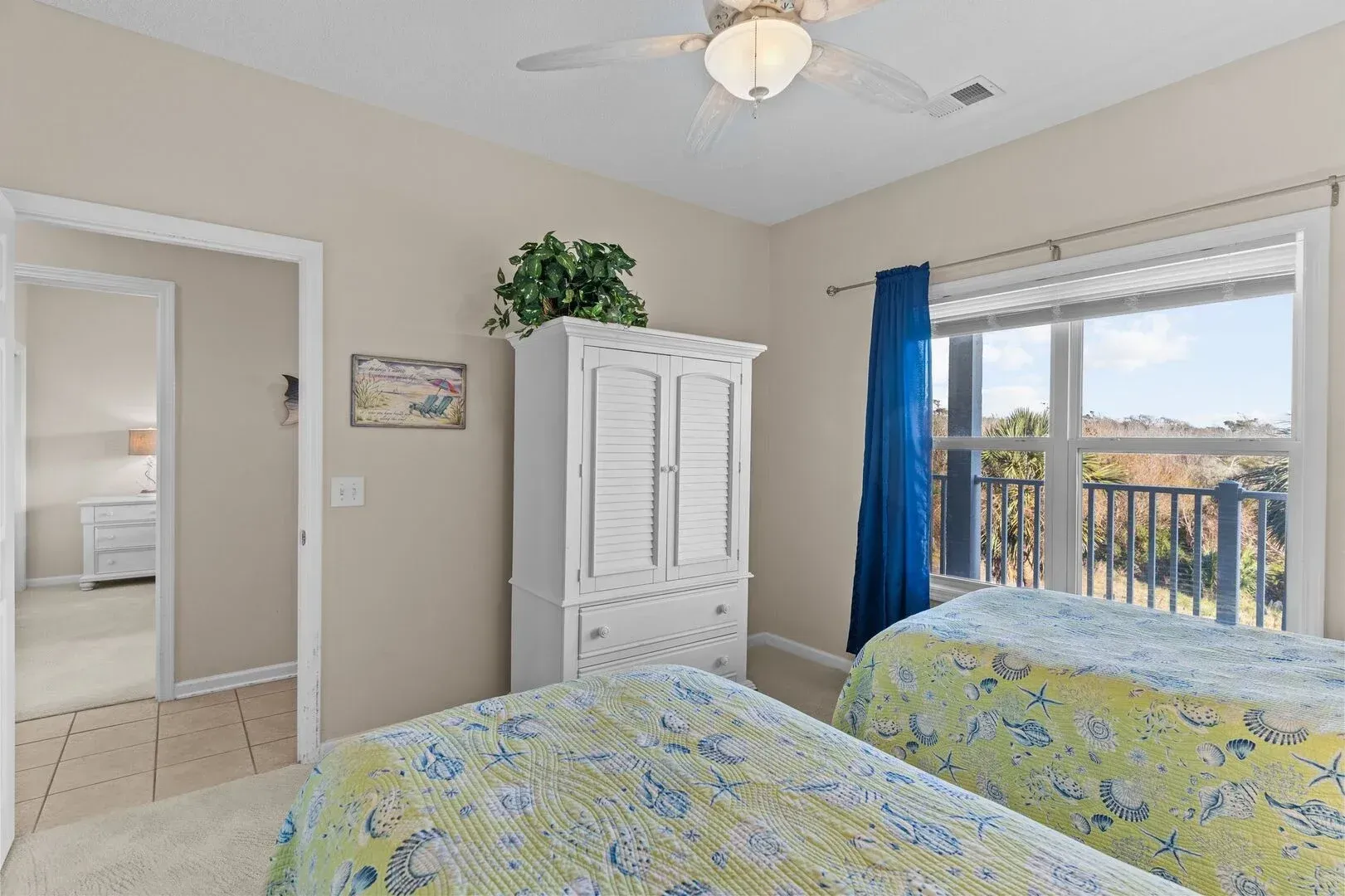 Bright bedroom with twin beds, white cabinet, and sliding door to balcony with ocean view.